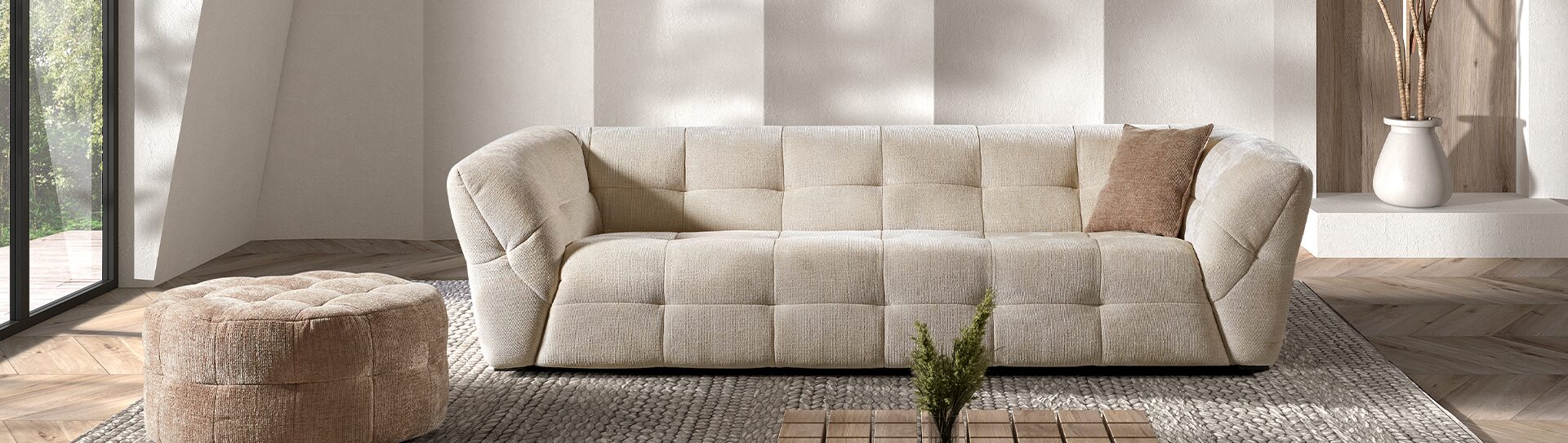Canapé droit DAISY Canapé 2,5 places beige matelassé et rembourré dans un salon sur un tapis gris et devant un mur blanc avec une ombre d'une feuille de palmier