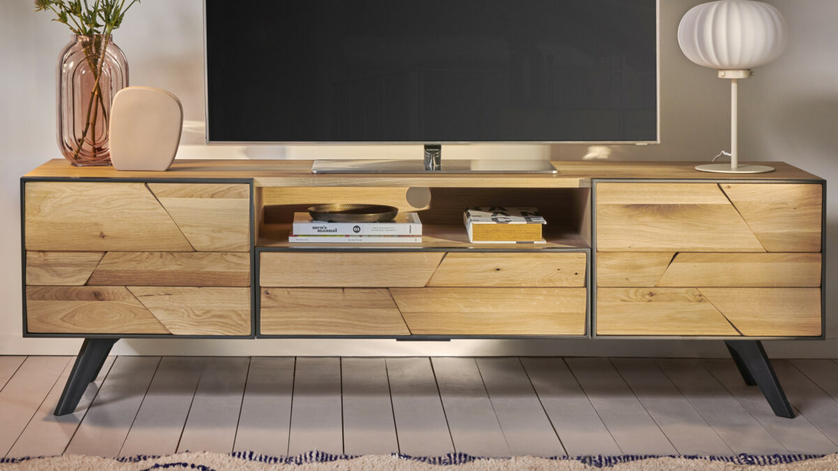 Meuble TV bas en bois massif à façade géométrique avec cadre noir, posé sur pieds inclinés, agrémenté de décoration, livres et lampe design dans un salon cosy.