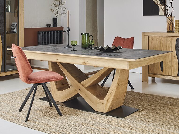 table à manger moderne en bois avec un plateau sombre et un piètement original en forme de X entrelacés, entourée de chaises rouges sur un tapis en jute, dans une salle à manger contemporaine avec buffet assorti.